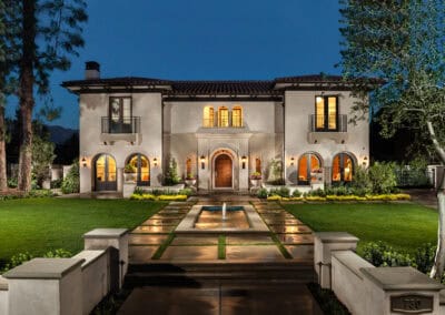 Elegant Mediterranean-style villa with lush gardens and warm lighting at night.