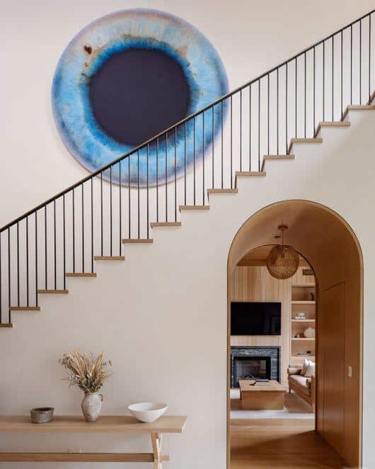 Blue circular wall art above staircase, wooden staircase with black railing, cozy living room visibl.