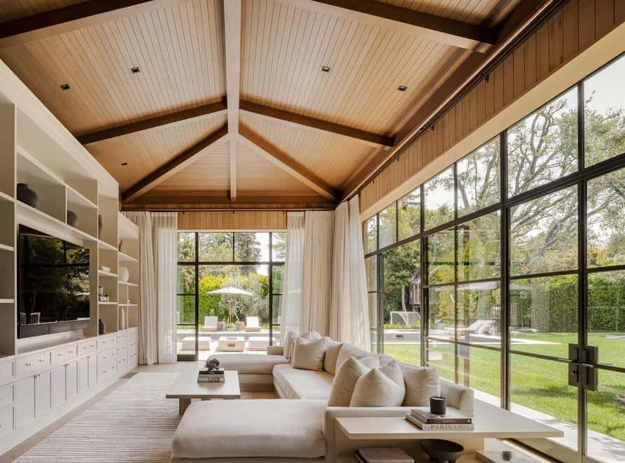 Spacious contemporary living room featuring large glass windows, wooden ceiling, and elegant white f.